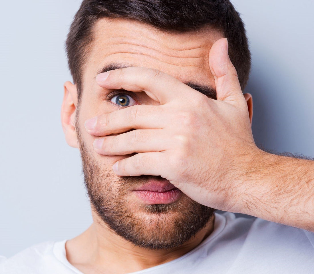 Man, face covered with hand, peaking out with one eye, confused about essential oils
