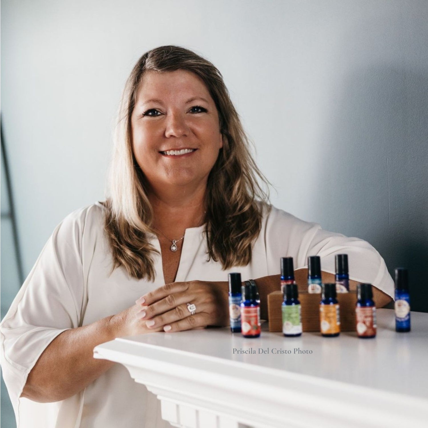 Sherrie Miller, founder of Essential for Wellness, standing at fireplace mantel with her organic essential oils brand for her About Me page.
